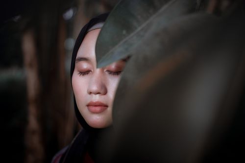 Free Close-up portrait of a woman with closed eyes and hijab partially obscured by a leaf. Stock Photo