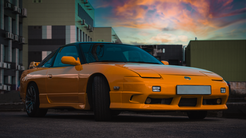 Free A luxurious yellow sports car parked in an urban setting with a vibrant sunset sky. Stock Photo