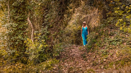 女人穿着蓝色连身衣走在森林里