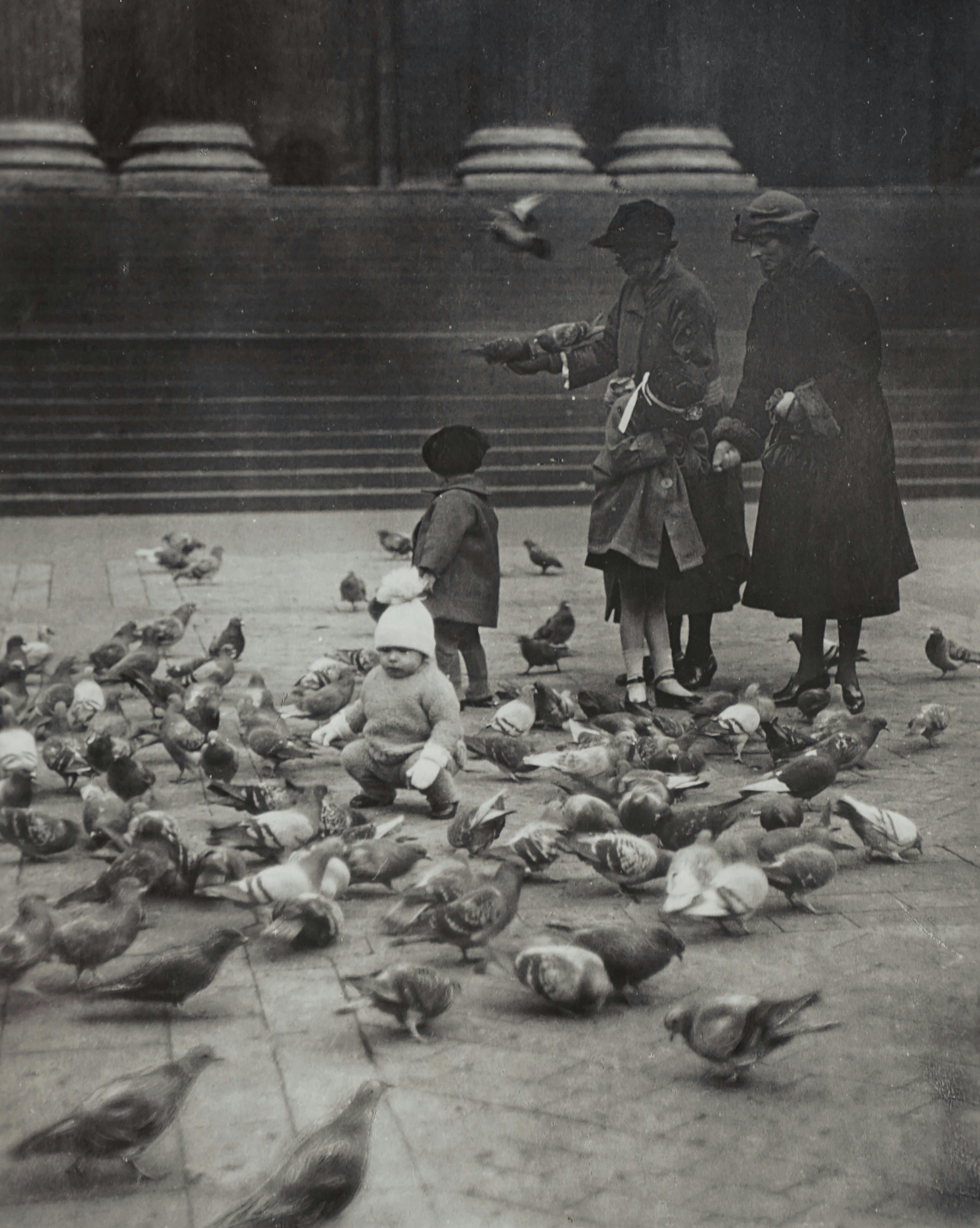 Historical black and white photo of a family feeding pigeons in London.