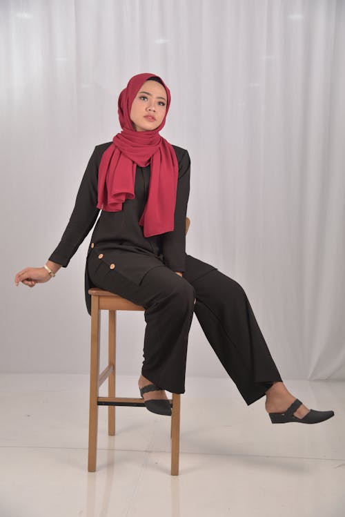 Woman in Black Long Sleeve Shirt and Red Hijab Sitting on Brown Wooden Seat