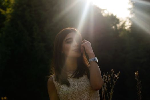 A serene portrait of a woman standing outdoors in sunlight with natural greenery backdrop.