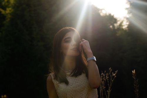 Free A serene portrait of a woman standing outdoors in sunlight with natural greenery backdrop. Stock Photo