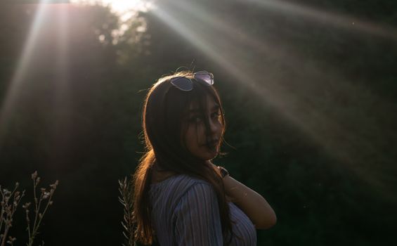 Woman with sunglasses in nature, sunlight streaming through trees.