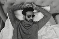 一位时尚男模特戴着太阳镜，躺在单色房间的床上