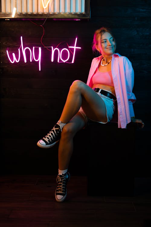 Woman in Pink Blazer and Black and White Striped Mini Skirt Sitting on Brown Wooden Floor