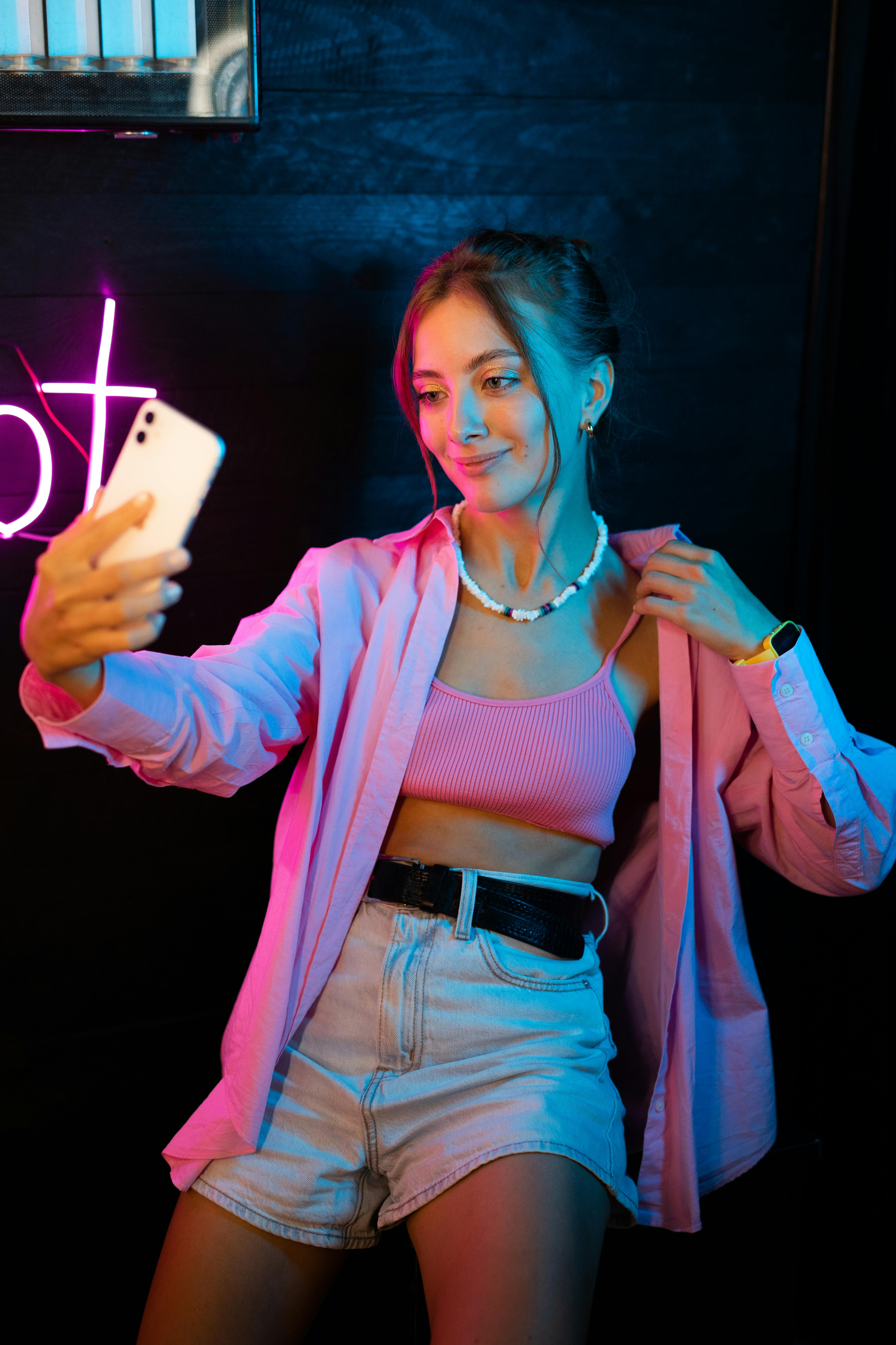 Stylish young woman taking a selfie with neon lighting in a fashionable indoor setting.
