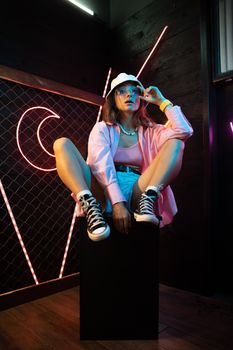 Stylish woman in a neon-lit room wearing Converse, embracing urban youth culture.