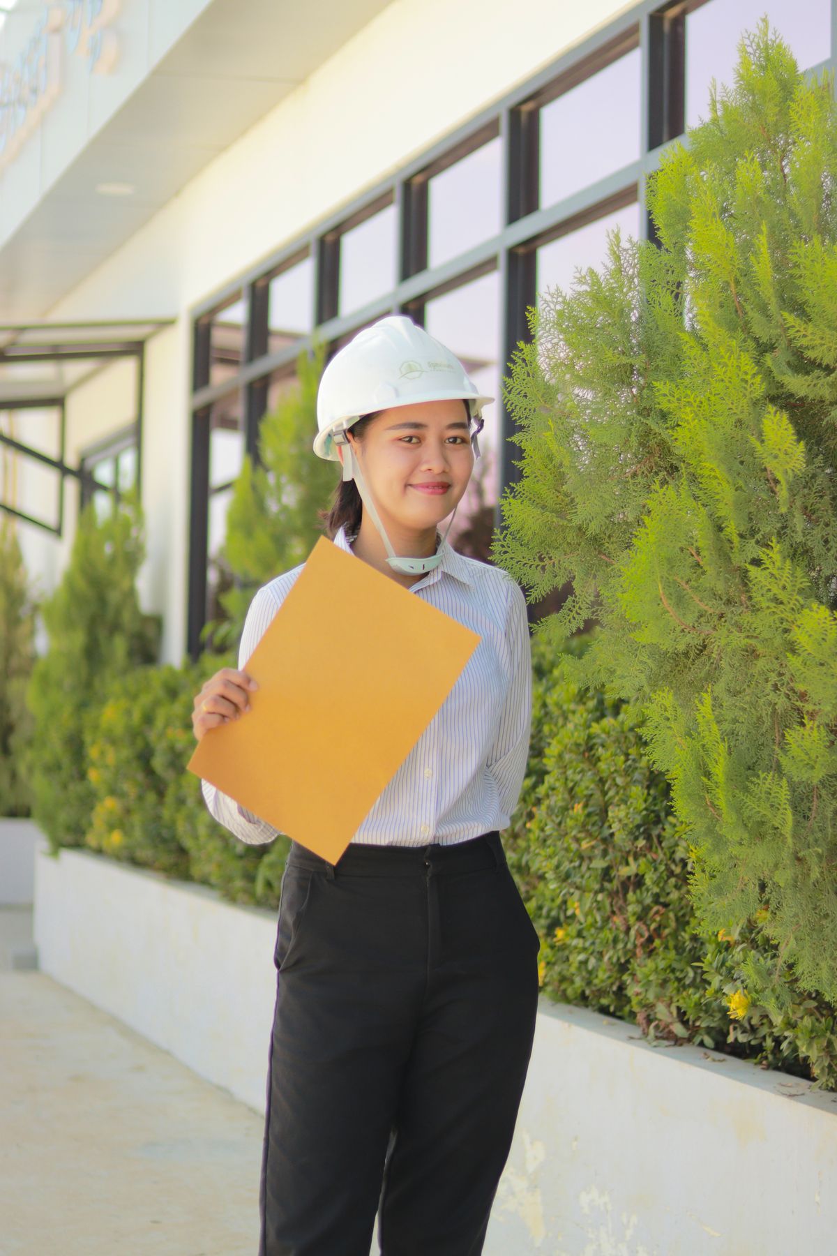 Asian female engineer in a hard hat holding project documents outdoors while reviewing equipment costs
