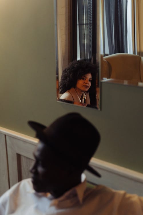 Reflection of a Woman in the Mirror Behind a Man Sitting on Chair Wearing Fedora Hat