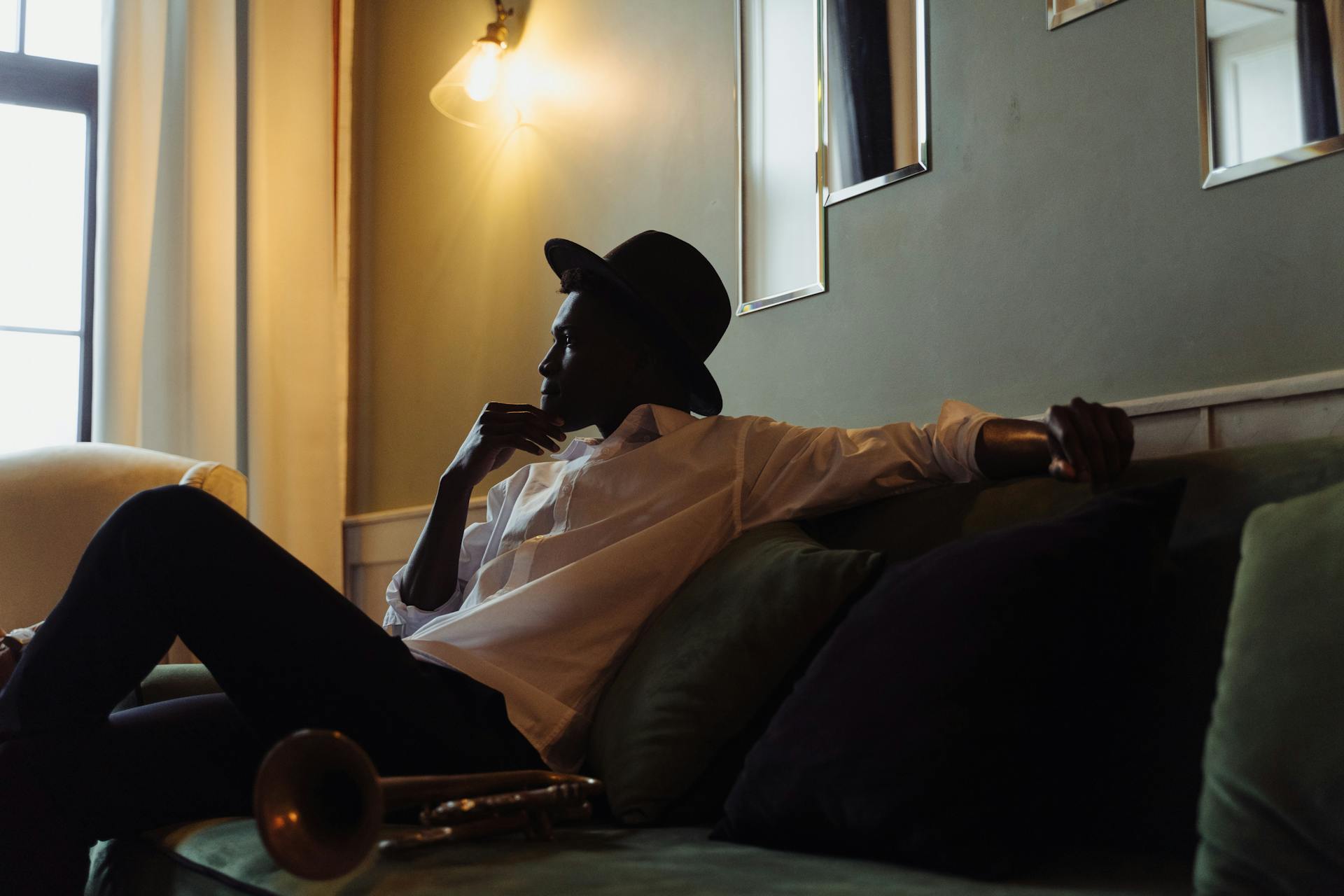 Casual portrait of a musician relaxing on a sofa with a trumpet and fedora hat.