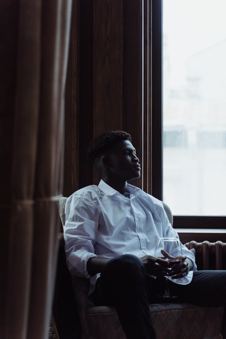 A Man Holding A Glass Of Wine While Sitting On A Couch