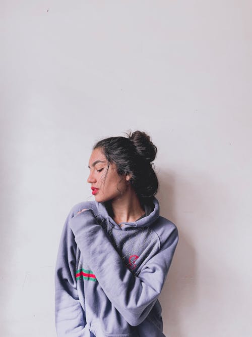 Woman in Gray Hoodie Leaning on White Wall