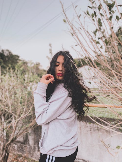 Woman with Curly Hair Wearing Gray Sweater while Standing Near Green Plants