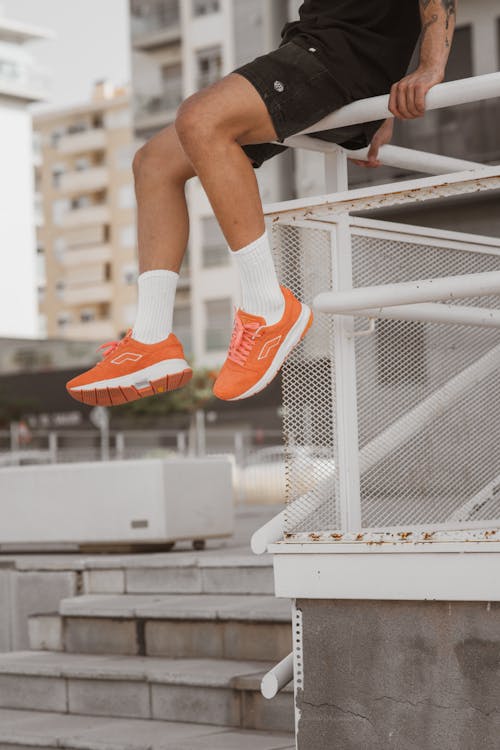 Person in Orang  Sneakers Sitting on a Handrail