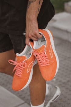 A person holding stylish orange sneakers, showcasing a sporty and vibrant style.