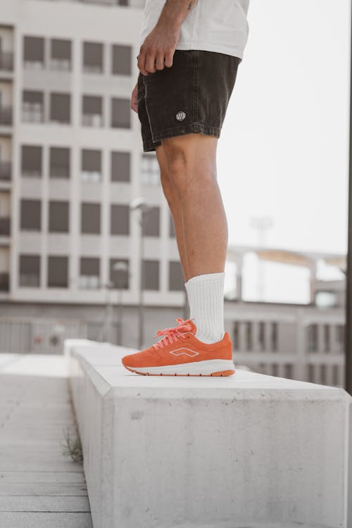 Person in Orange Sneakers and Black Shorts Standing on Concrete 