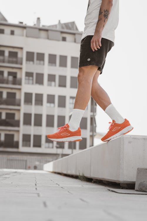 Person in Black Shorts and Orange Sneakers Standing on Concrete Block