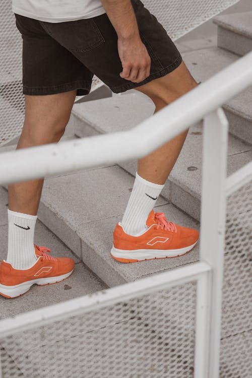 Free Person in Orange Sneakers and Black Shorts Going Up the Stairs Stock Photo