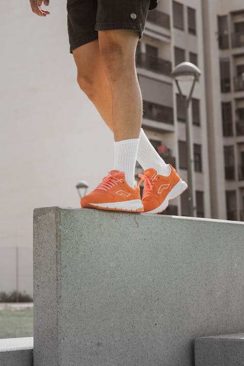 Person in Orange Sneakers and Black Shorts Walking on Concrete Block