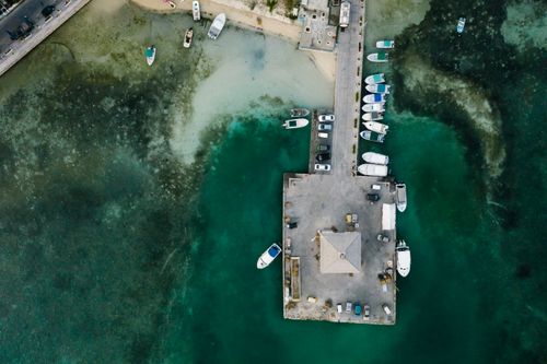 Free High-angle aerial shot of a coastal dock, with several boats moored in turquoise waters. Stock Photo