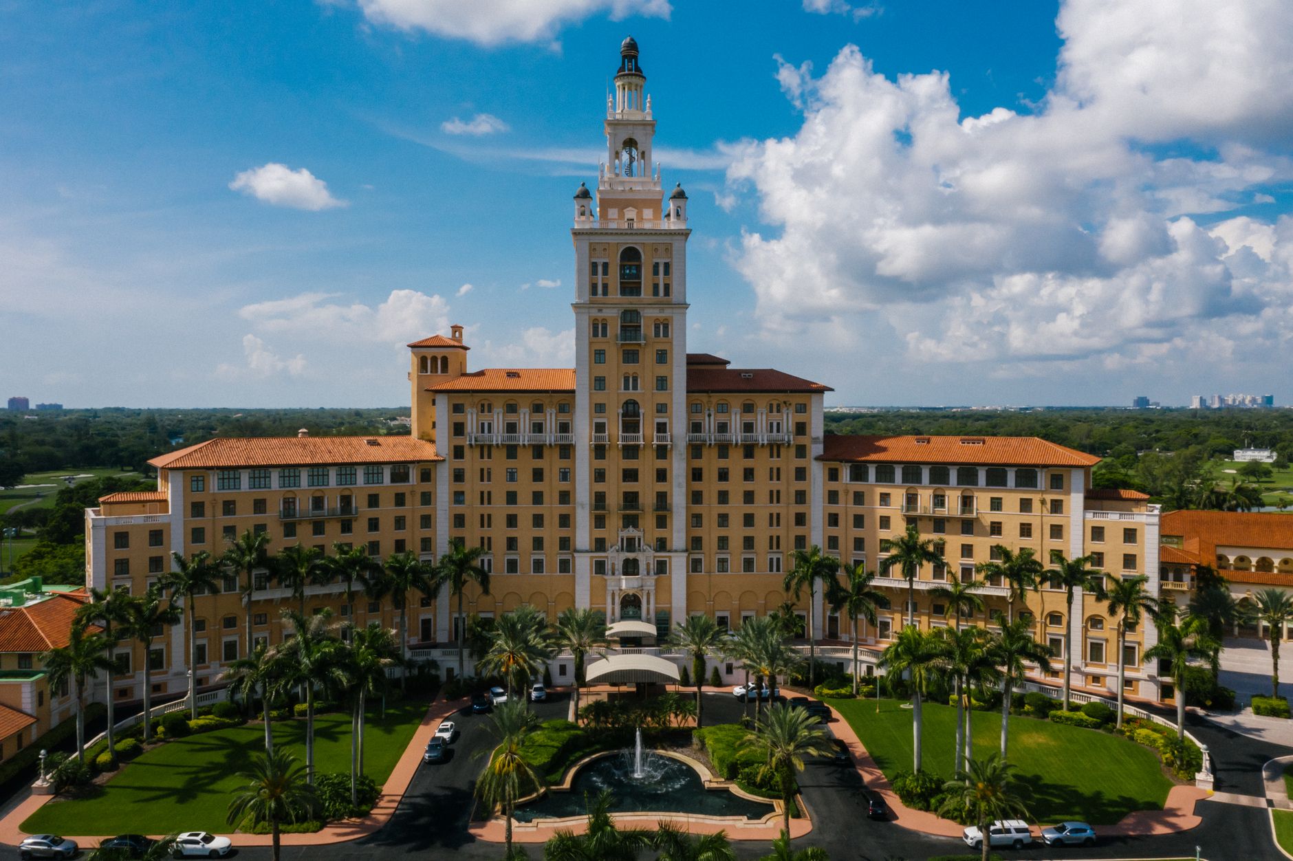 Majestic aerial view of the iconic hotel surrounded by lush palm trees and a clear blue sky.