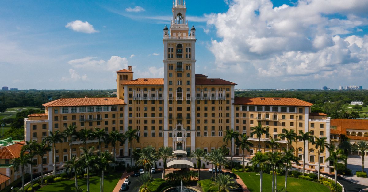 Majestic aerial view of the iconic hotel surrounded by lush palm trees and a clear blue sky.
