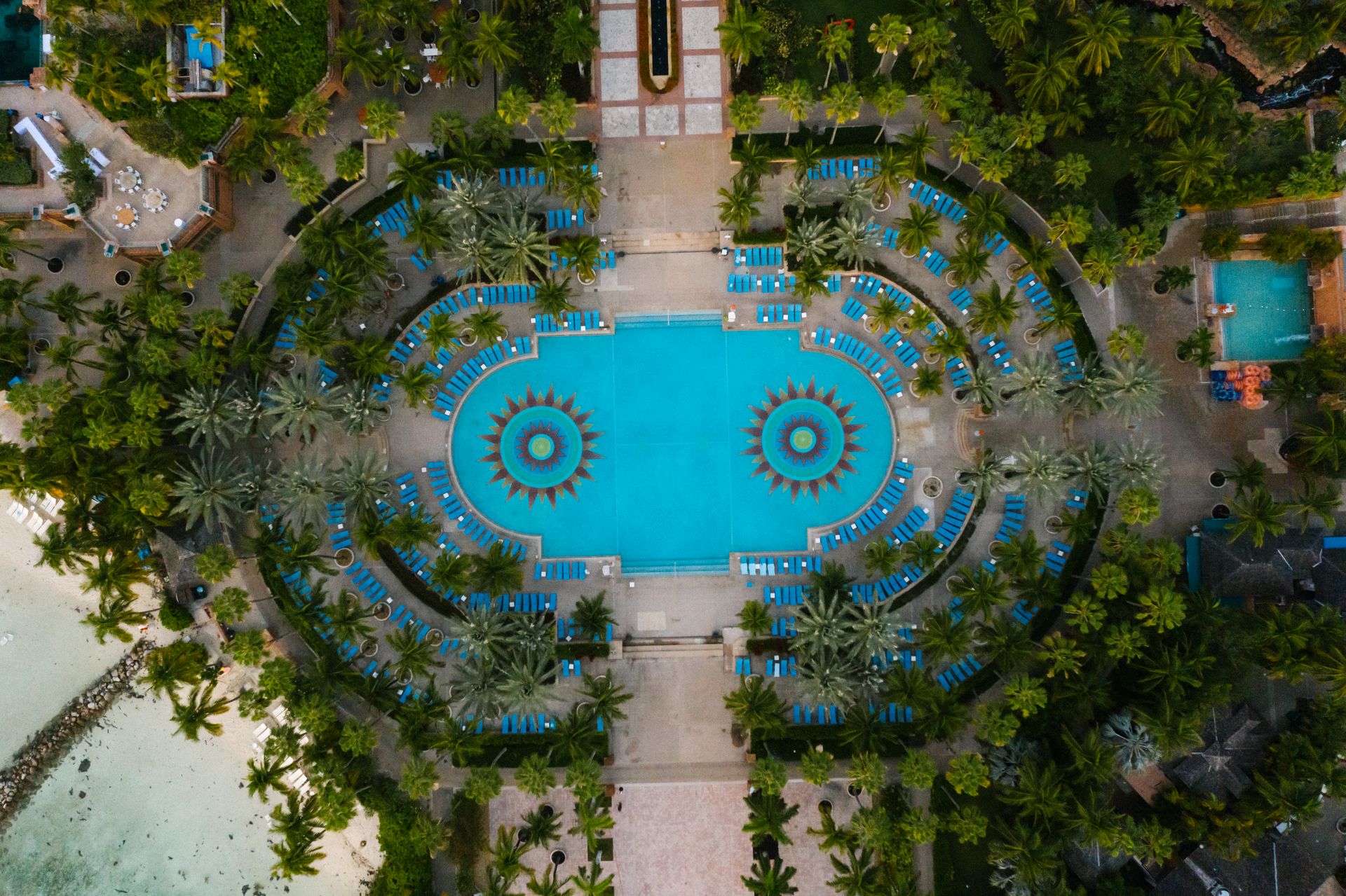 Stunning aerial view of a luxurious resort pool surrounded by lush greenery and blue loungers.