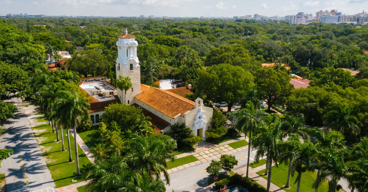 Aerial photo of a church in Coral Gables, Miami, surrounded by lush trees and urban landscape.