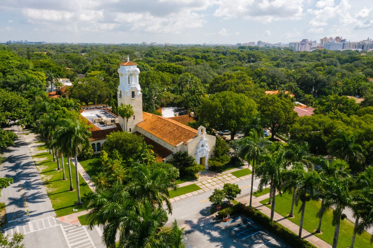 Aerial view of Coral Gables: a white bell tower, terracotta roofs and avenues of royal palms