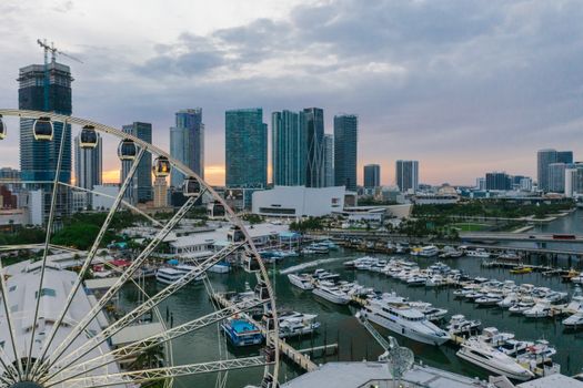 Aerial view of modern skyline with ferris wheel and marina in vibrant city at dusk.