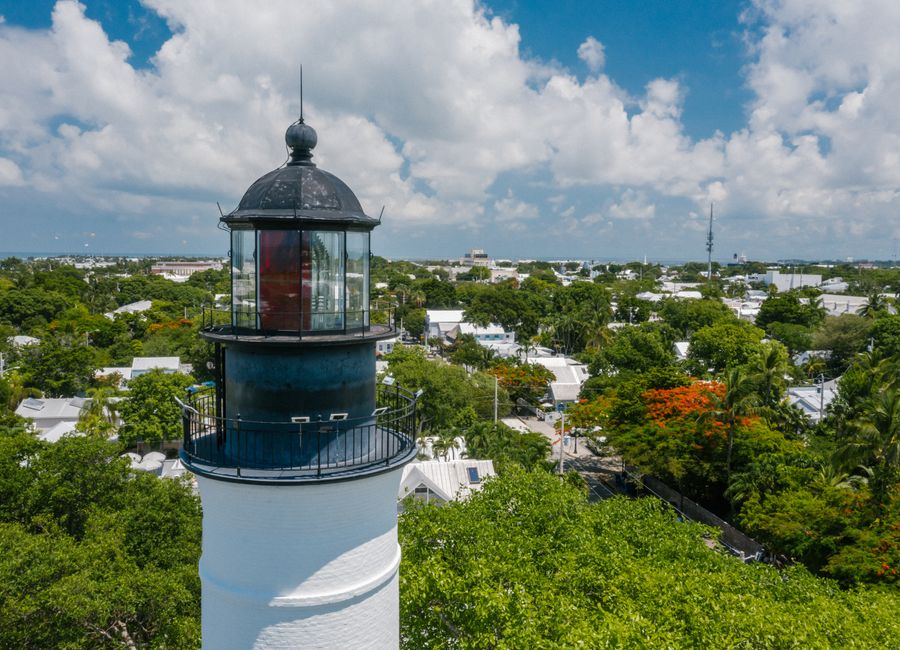 Discover the historic Key West lighthouse surrounded by lush greenery under a bright blue sky.