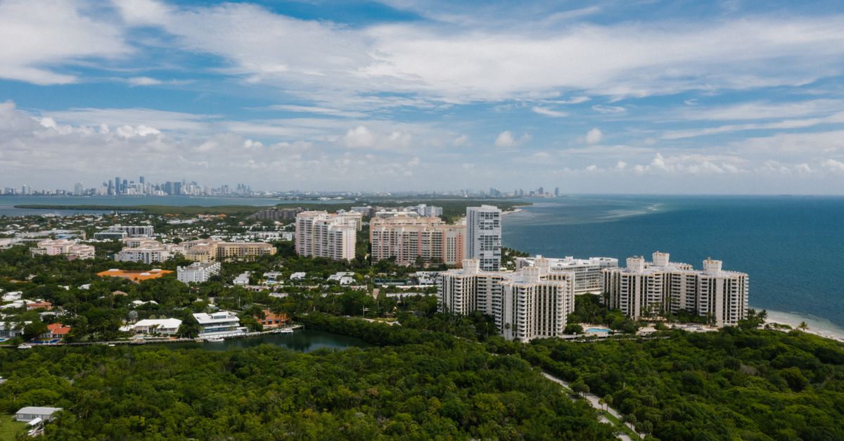 Aerial view of a coastal city with high-rise buildings overlooking the ocean under a clear blue sky.