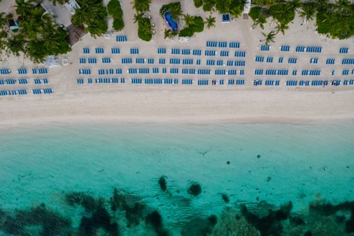 Free Stunning aerial view of a sandy tropical beach lined with blue lounge chairs and crystal-clear ocean waters. Stock Photo