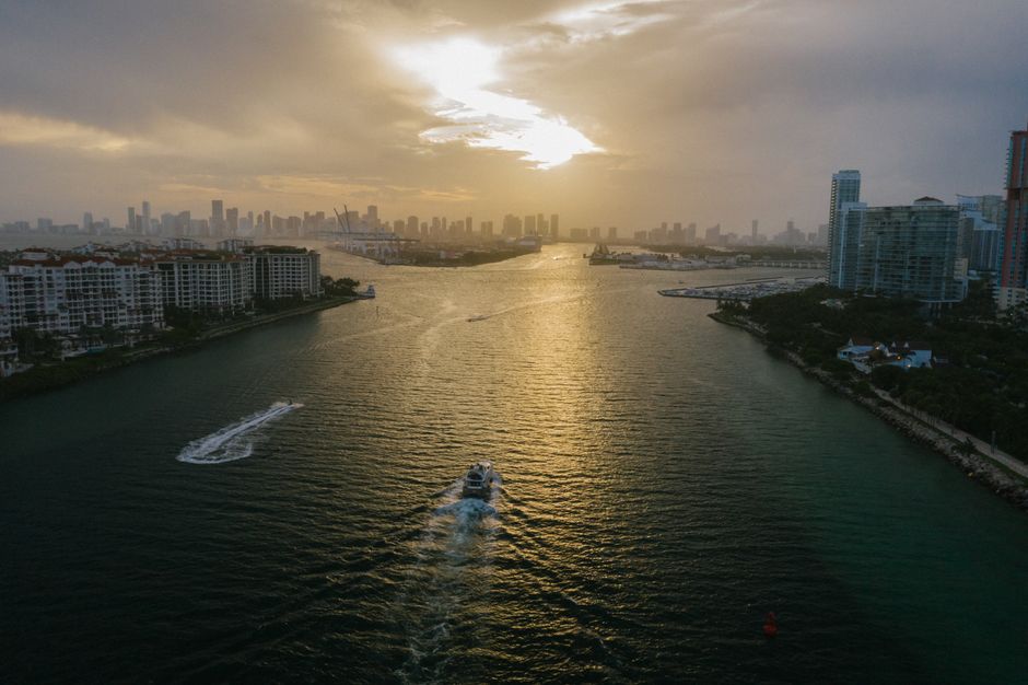 Stunning aerial shot of a boat sailing through a river against a city skyline at sunset, showcasing urban architecture.