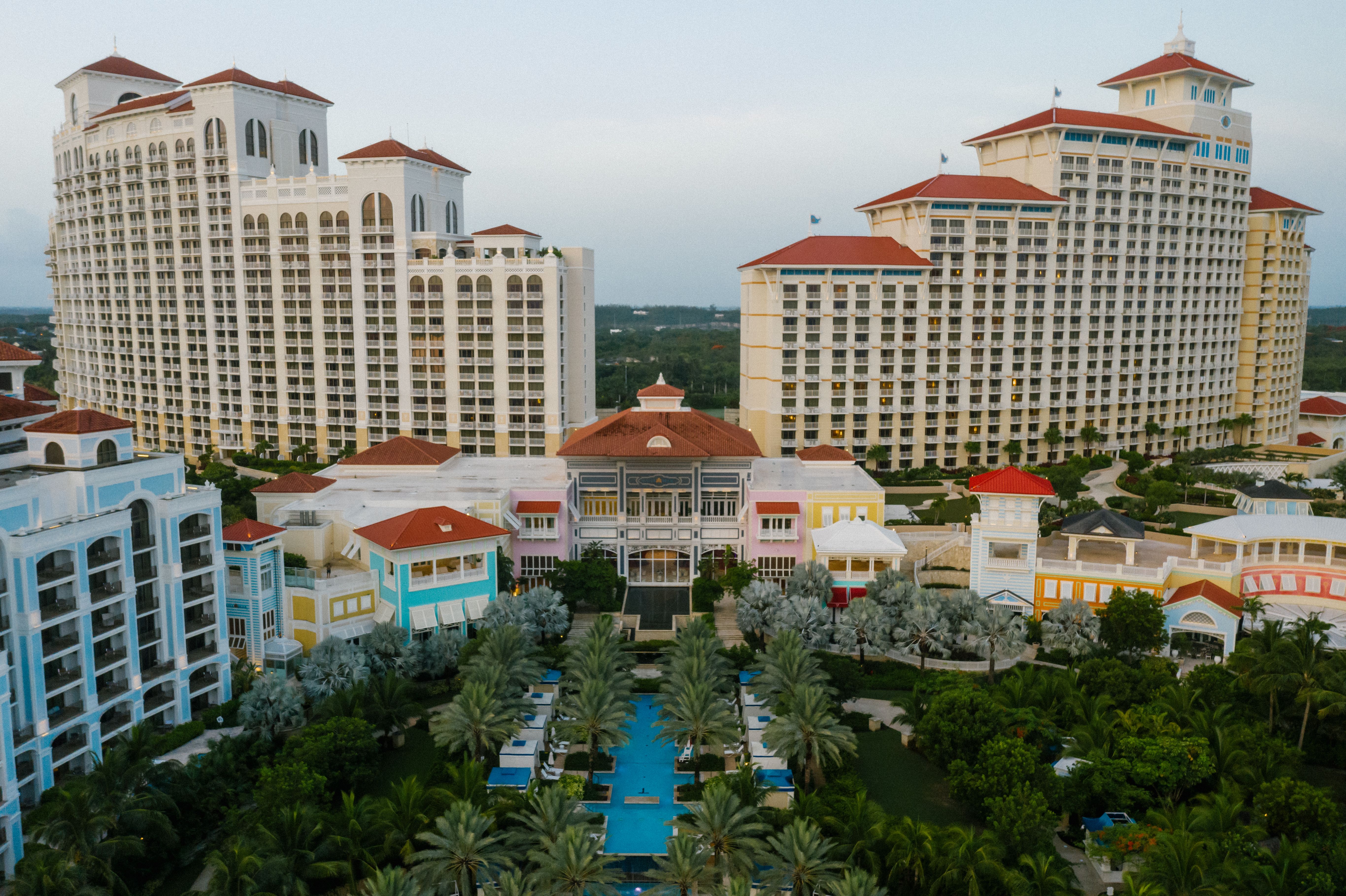 Aerial view of a luxury resort with high-rise towers, palm trees, and a central swimming pool.
