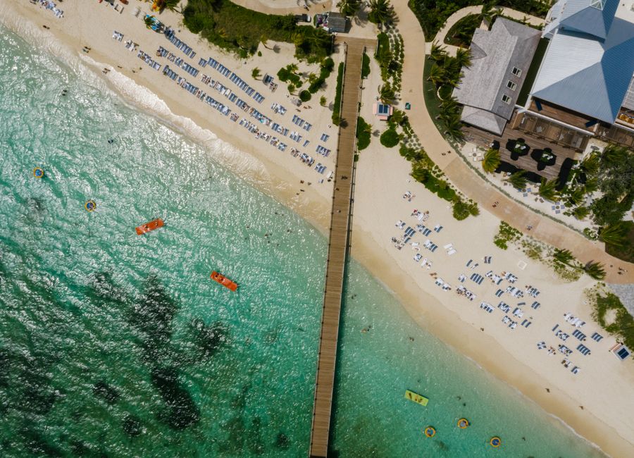 Stunning aerial shot of a sandy beach with clear turquoise waters and a wooden pier.
