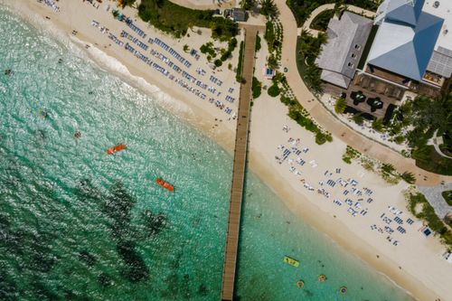 Free Stunning aerial shot of a sandy beach with clear turquoise waters and a wooden pier. Stock Photo
