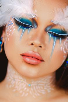 Close-up portrait showcasing creative eye makeup with feathers and artistic detailing in a dramatic style.