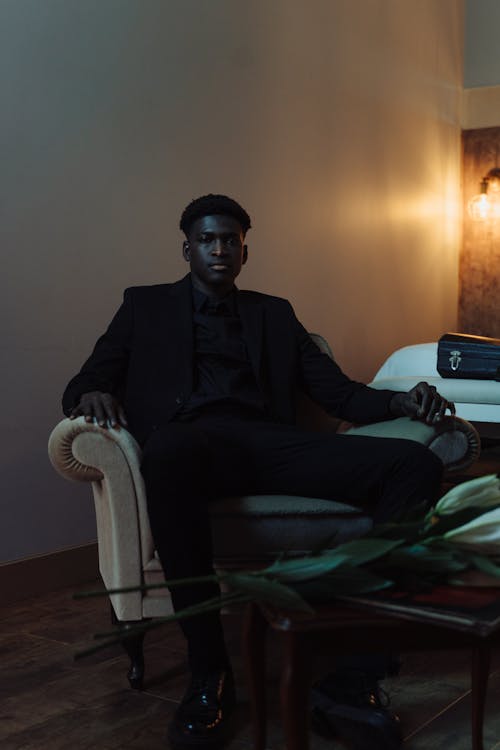 Man Wearing Black Suit while Sitting on Couch