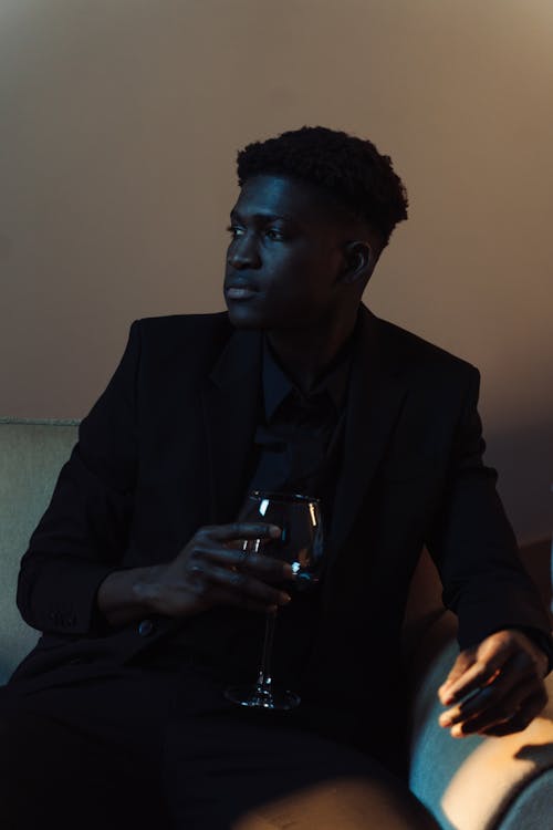 Man in Black Suit Sitting on Couch while Holding a Wine Glass