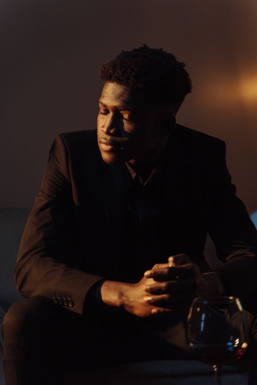 Free A thoughtful man in a black suit, sitting with a wine glass on a table, indoors. Stock Photo