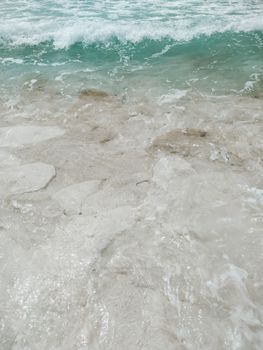 Close-up of clear turquoise waves washing over a serene sandy beach.