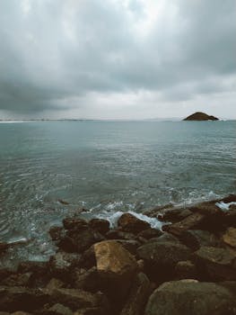 Serene view of a rocky shore against a calm sea under an overcast sky.