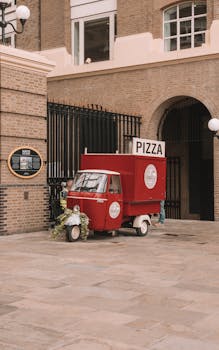A retro red pizza truck parked on a city street, offering a vintage urban vibe.