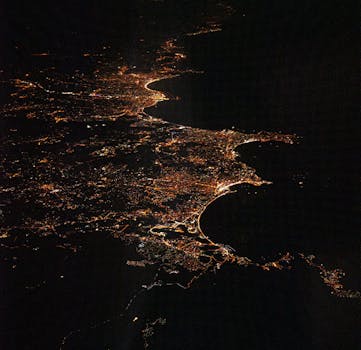 A breathtaking aerial night view showcasing illuminated cityscapes along the coastline.