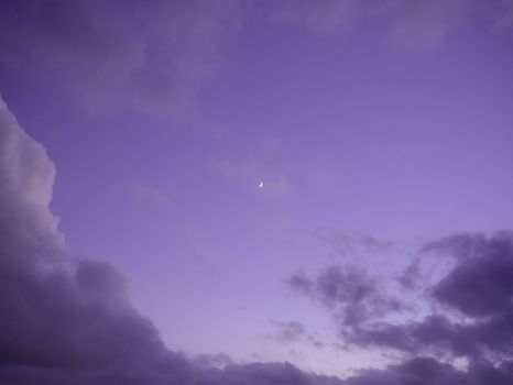 A serene purple sky with a crescent moon surrounded by clouds at twilight, photographed in Ajaccio, France.