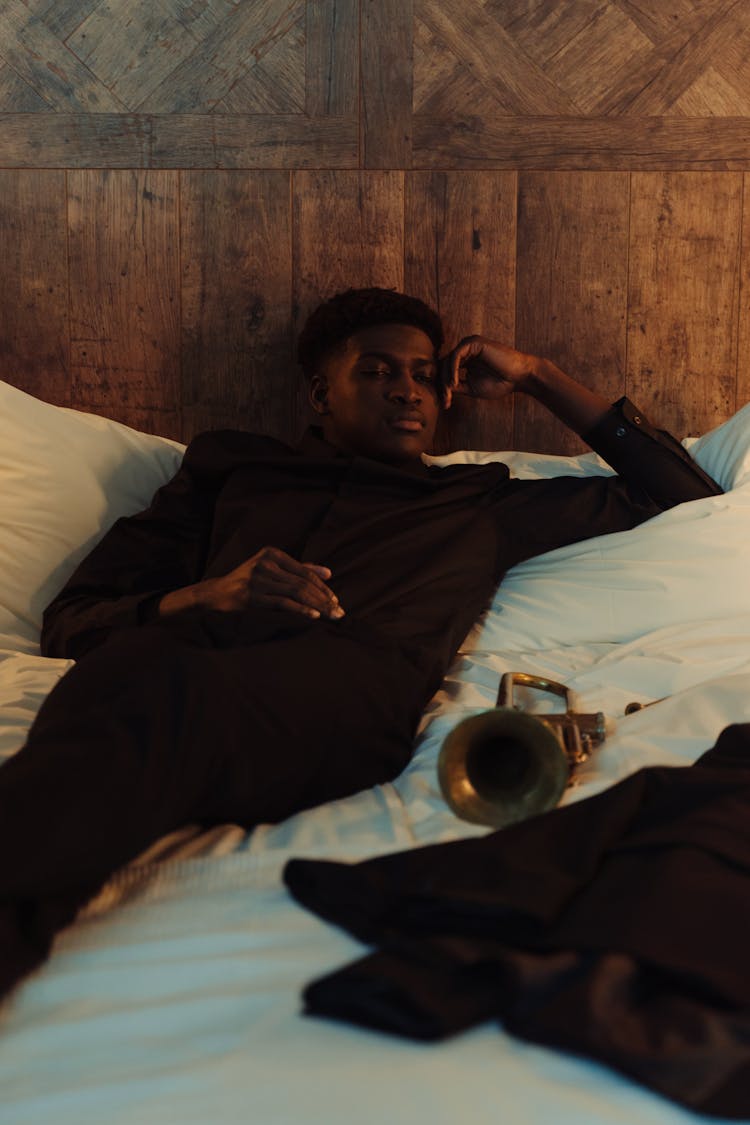 Man In Black Long Sleeves Lying On White Bed With His Trumpet