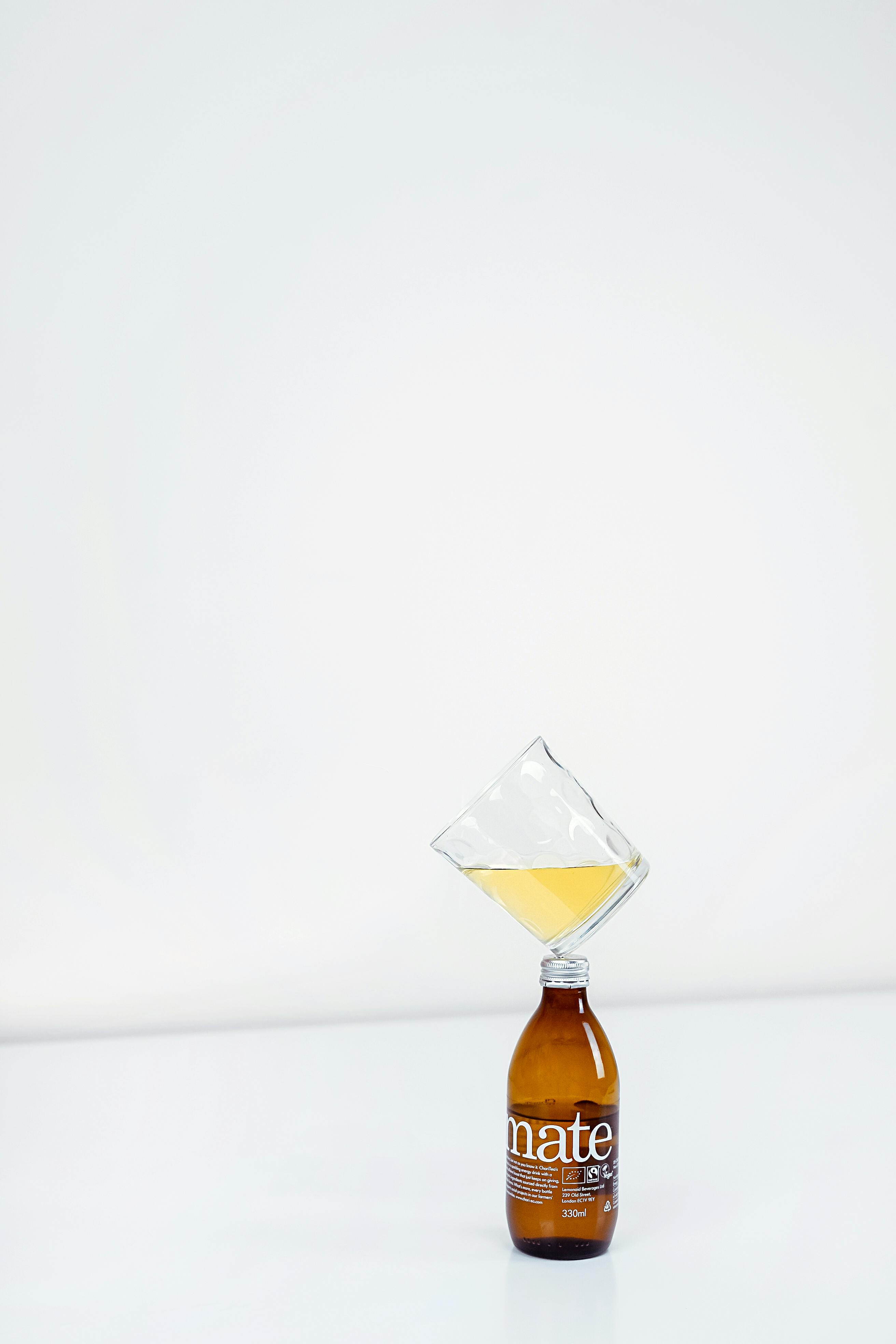 A minimalist photo featuring a balancing glass and bottle with a white background, showcasing creativity.