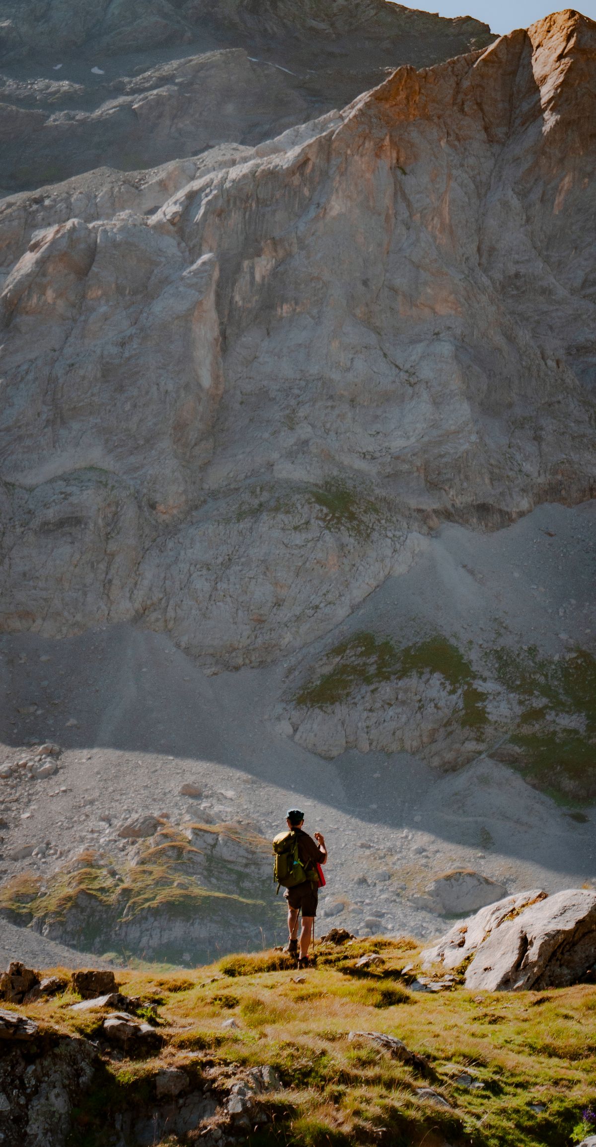 A lone hiker dwarfed by a vast Pyrenean rock wall